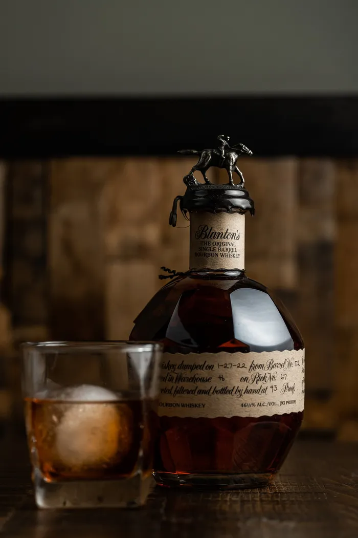A bottle of Blanton&rsquo;s bourbon beside a rocks glass with a large ice sphere