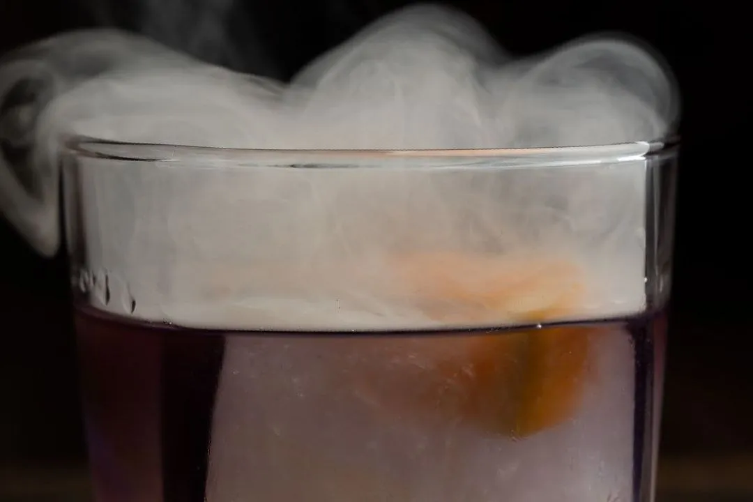 A smoked old fashioned in a rocks glass, wreathed in smoke