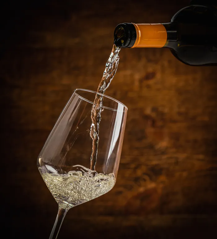 White wine being poured into a glass against a warm wooden backdrop