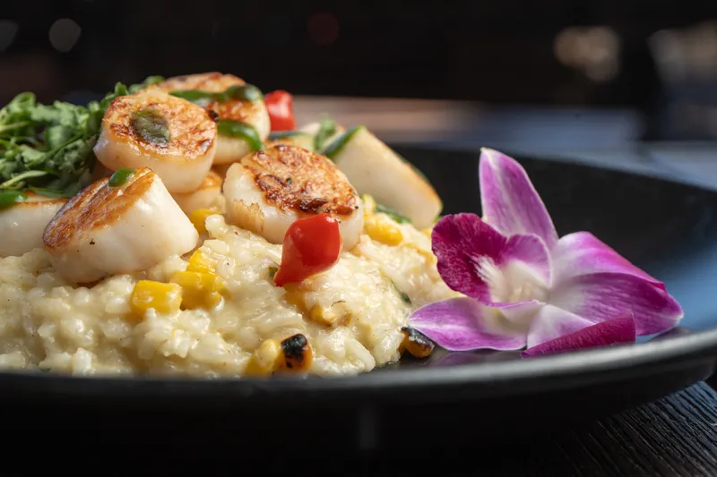 Pan-seared scallops over sweet corn risotto with an orchid garnish