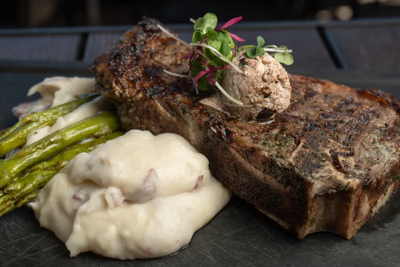 Grilled bone-in steak topped with herb butter beside whipped potatoes and asparagus