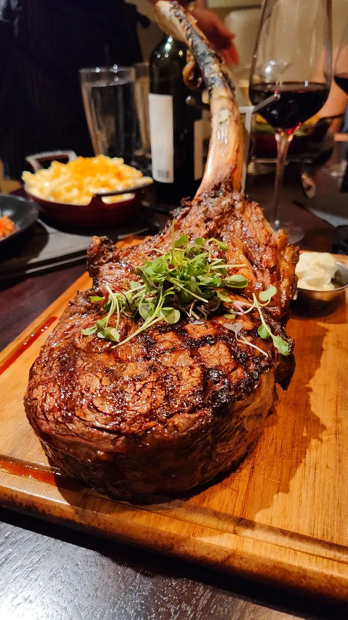 A grilled bone-in tomahawk steak served with sides on a wooden board