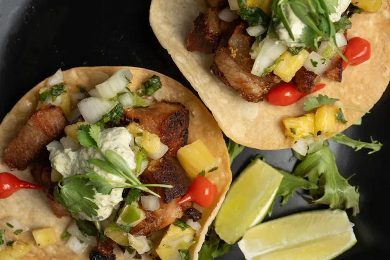 Tacos topped with crisp pork, pineapple salsa and lime