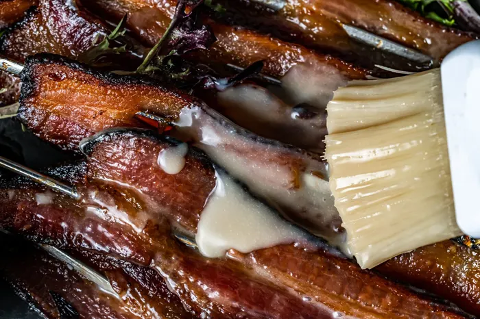 Candied bacon being brushed with a sweet glaze