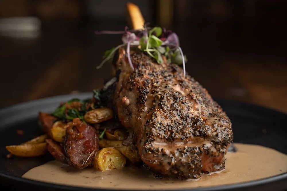 Pepper-crusted bone-in steak over roasted potatoes with a creamy sauce